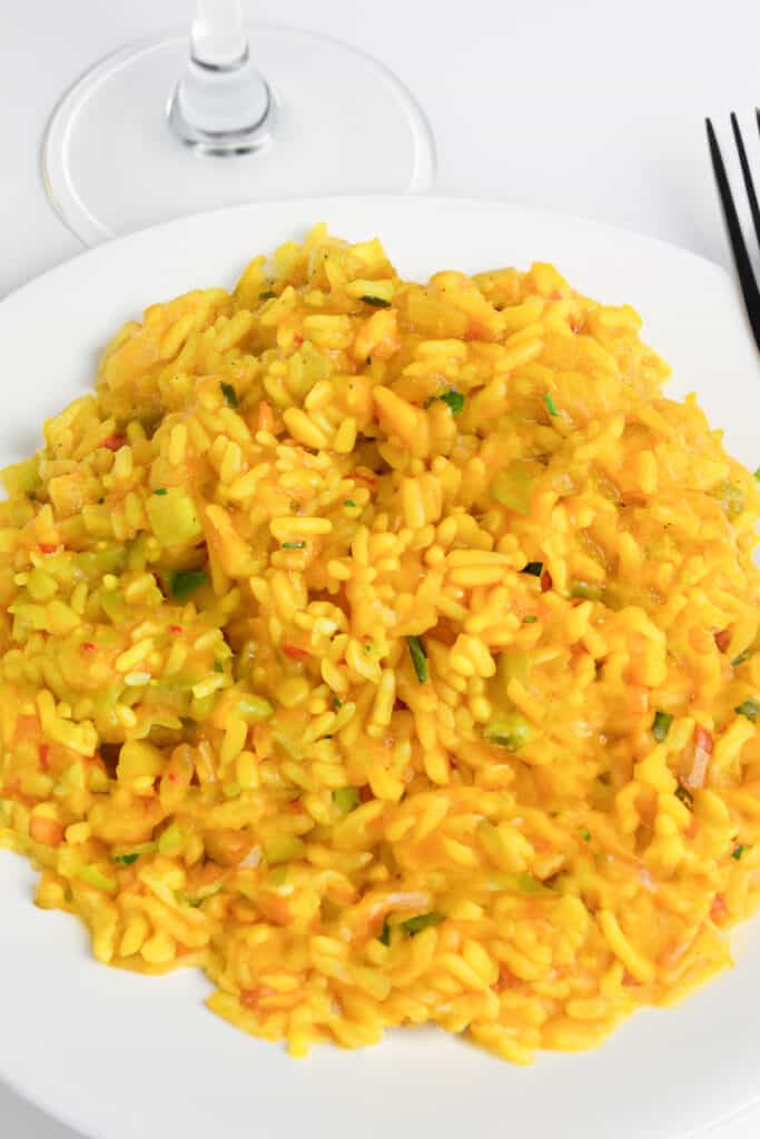 an overhead image of Saffron Risotto on a plate with a fork and wine glass in the background