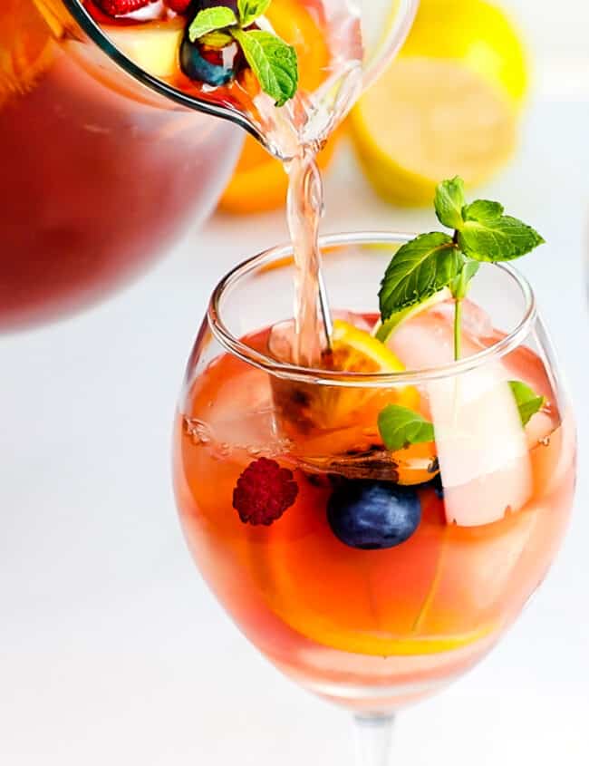 a pitcher of Rosé Sangria with fresh fruit being poured into a glass with ice.