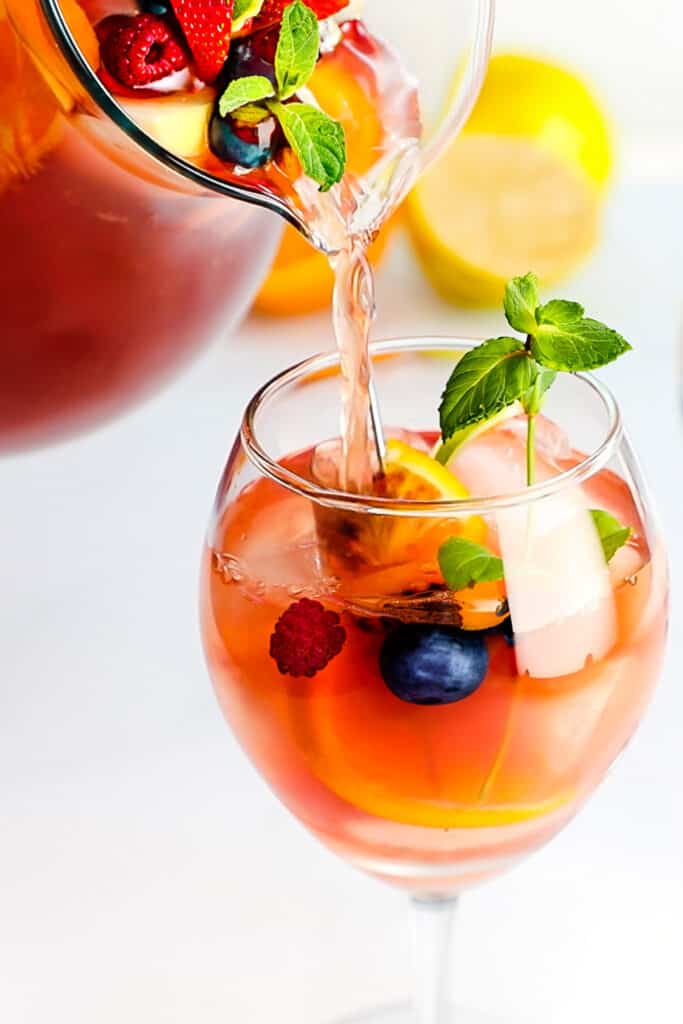 a pitcher of Rosé Sangria with fresh fruit being poured into a glass with ice.