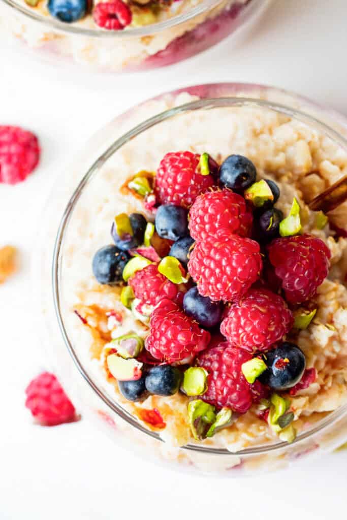 a close up image of a jar filled with overnight oatmeal and topped with mixed berries and chopped pistachios