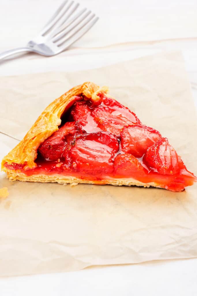 a slice of a Strawberry Galette on baking paper with forks in the background.
