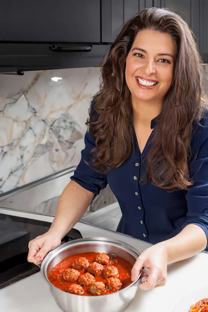 Erren of Erren's Kitchen holding a pot of meatballs in tomato sauce.