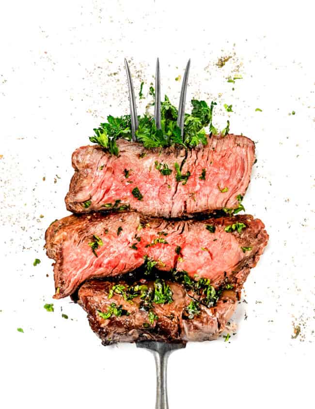 a serving fork with three strips of thick cut grilled filet mignon garnished with parsley.