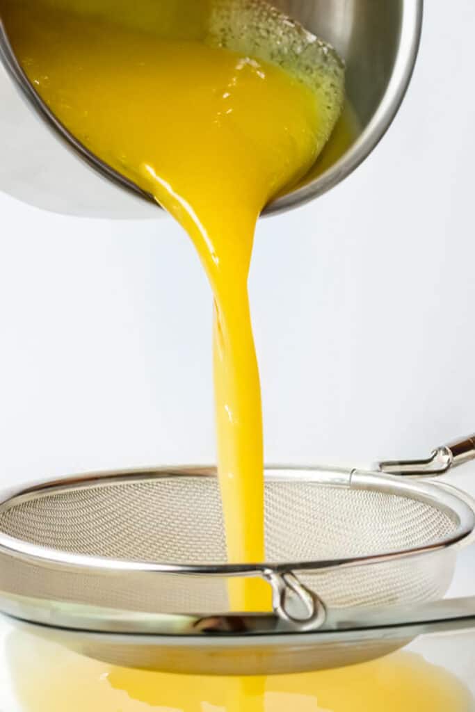 lemon curd being poured through a sieve.