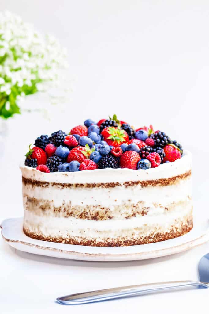 the uncut cake with semi-naked sides and topped with mixed berries.