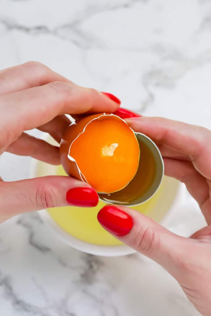 a woman Separating the yolk from the white of a brown egg.