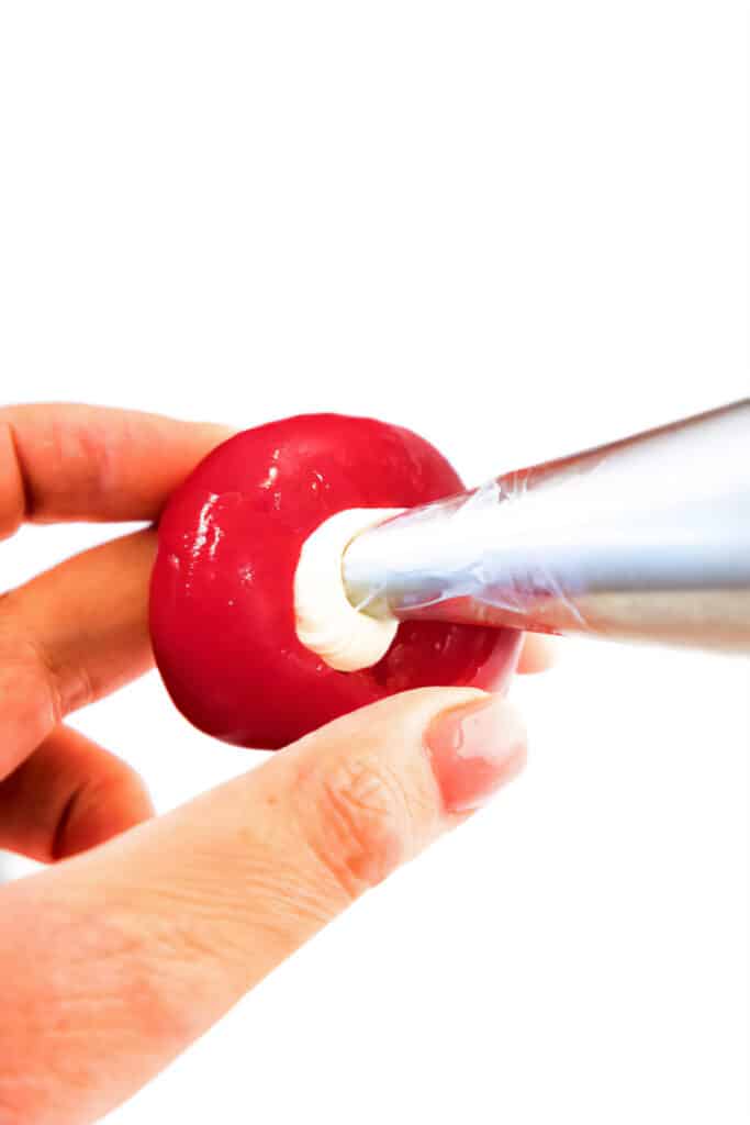 a piping bag filling a cherry pepper with the cream cheese filling.