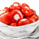 a white marble bowl of Stuffed Cherry Peppers and a cloth napkin under the bowl.