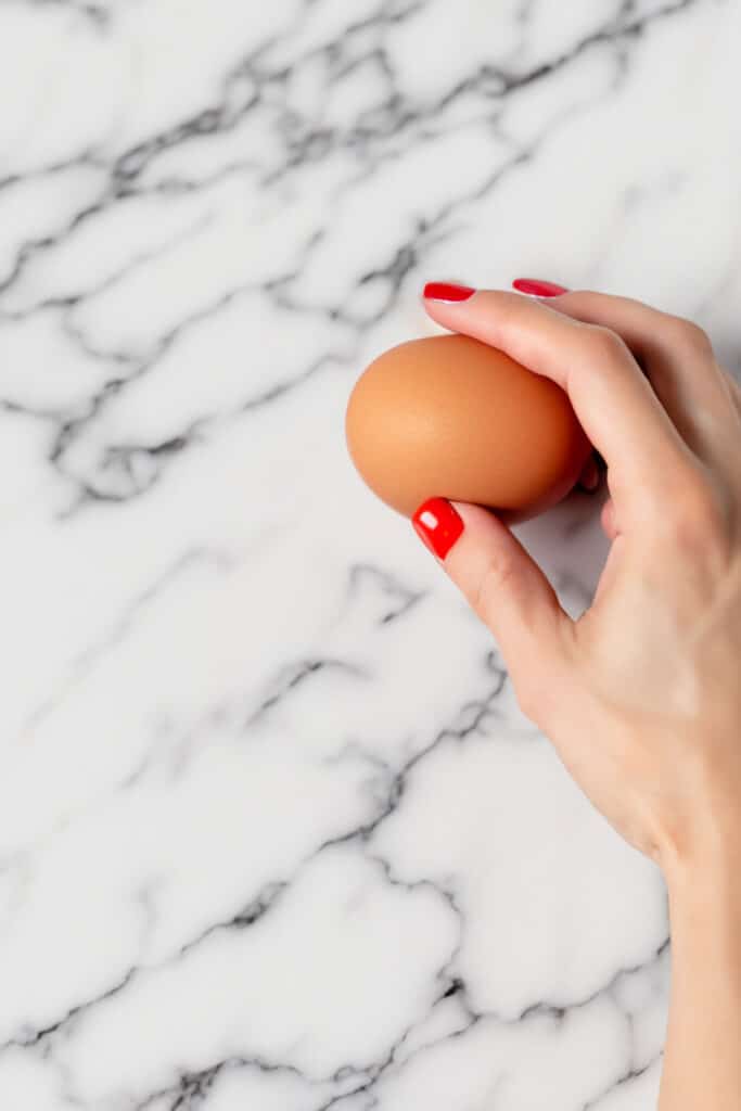 a woman tapping an egg on a white countertop.