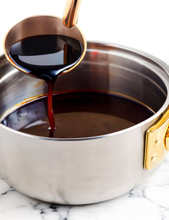 a ladle pouring red wine sauce into a saucepan