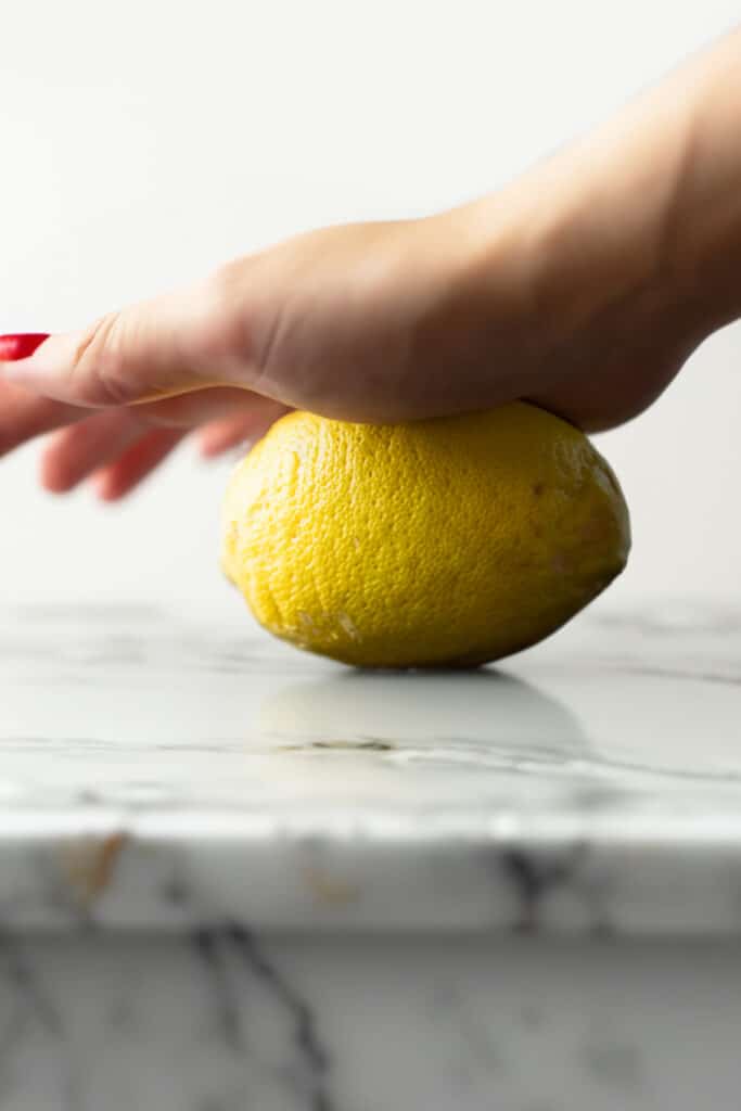 a woman's hand rolling a lemon on a kitchen counter.