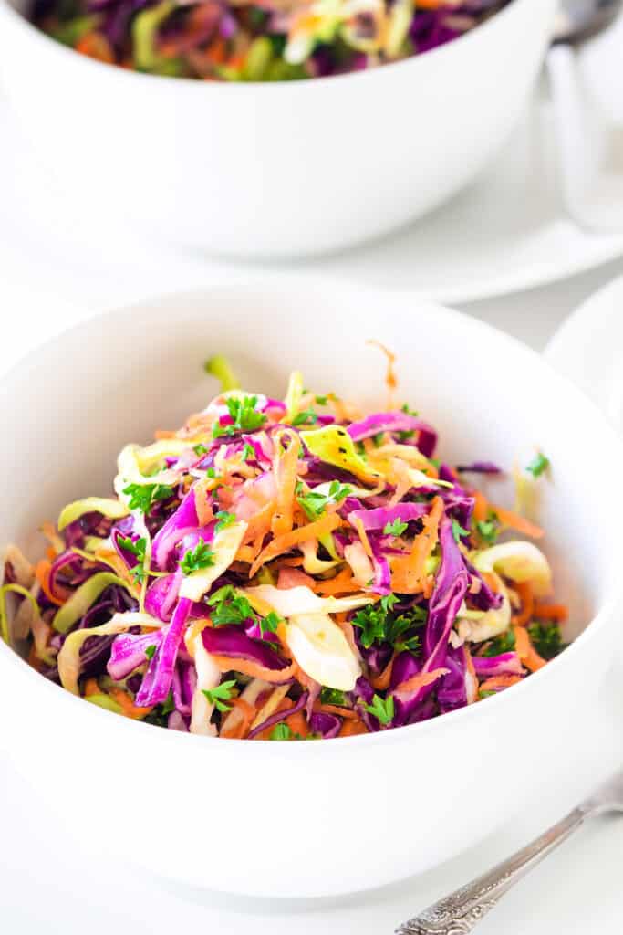 a bowl of vinegar coleslaw with the serving bowl in the background with a spoon.