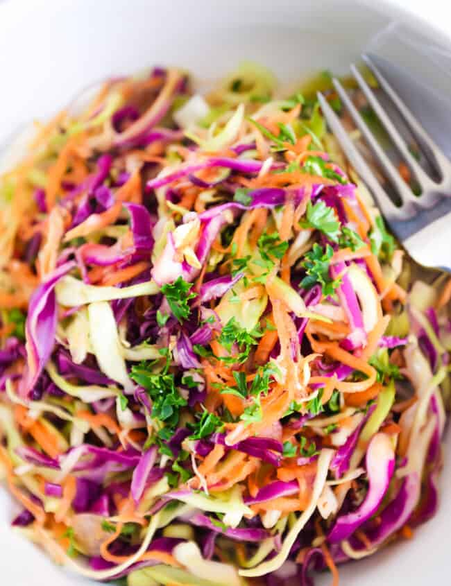 a close up image of vinegar coleslaw in a white bowl with a fork