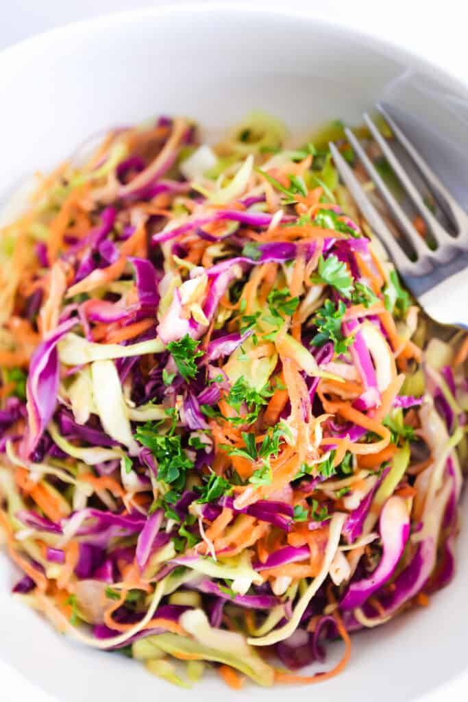 a close up image of vinegar coleslaw in a white bowl with a fork