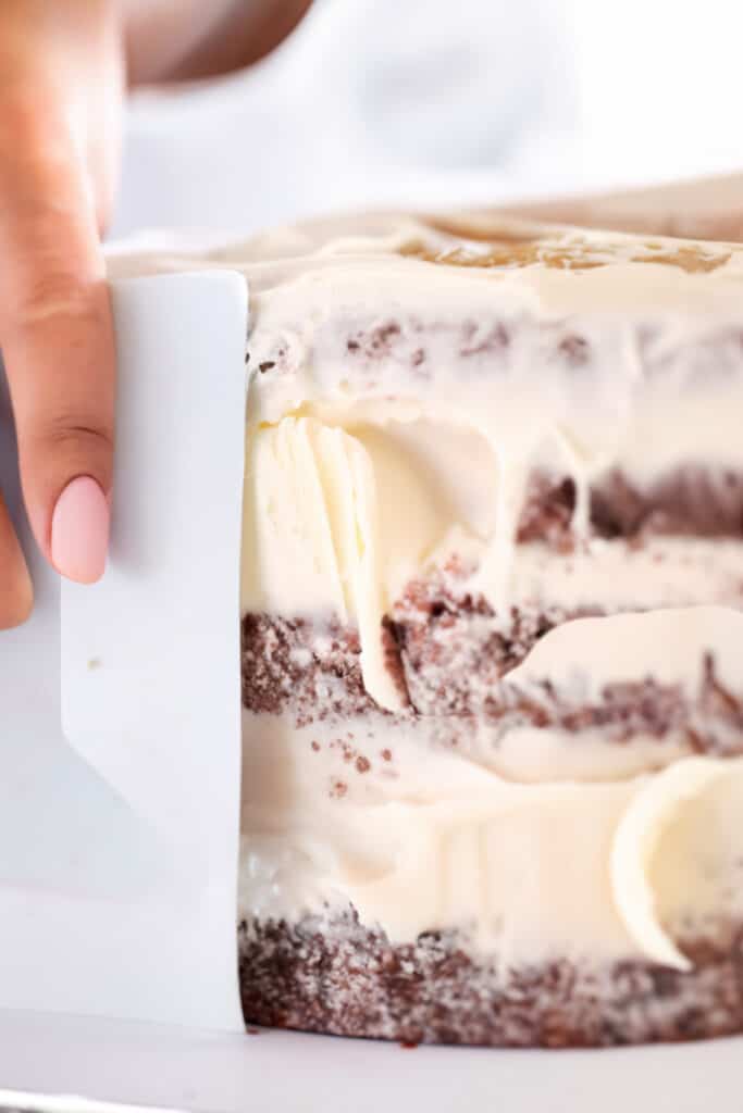 a bench scraper scraping frosting on the side of the cake.