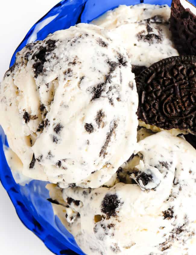 a blue glass dessert bowl with scoops of cookies and cream ice cream garnished with broken cookies.