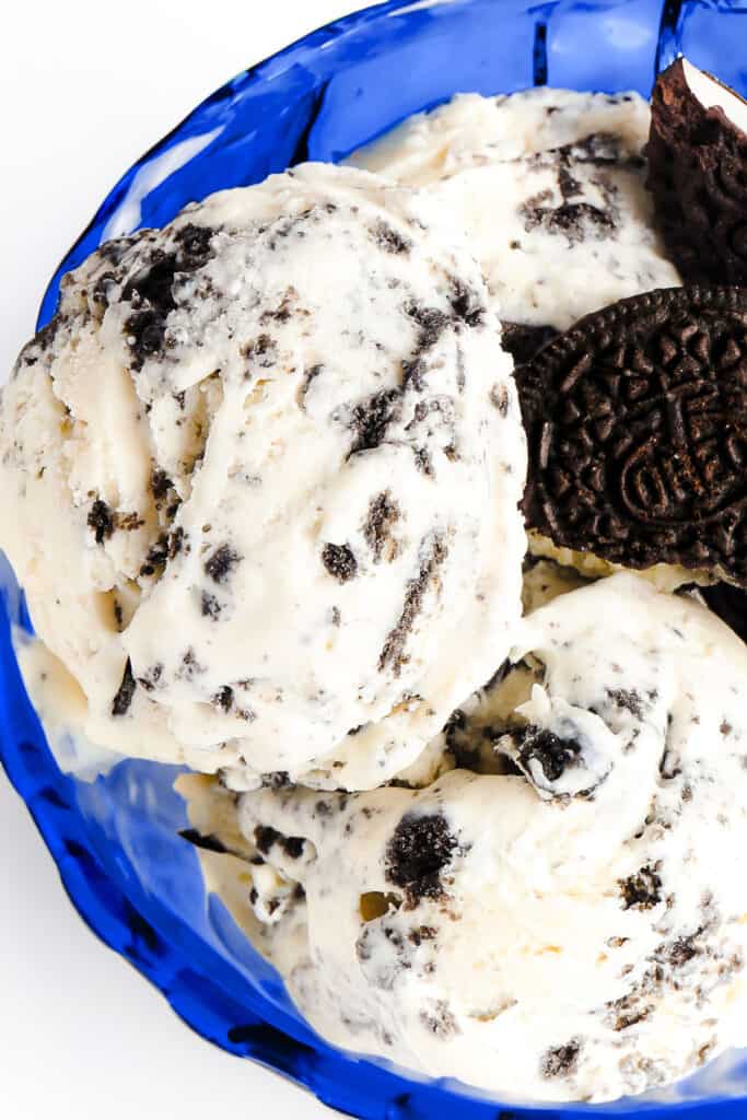 a blue glass dessert bowl with scoops of cookies and cream ice cream garnished with broken cookies.