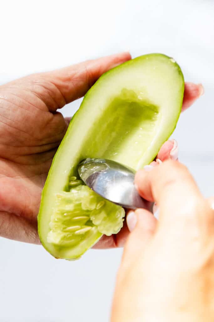 a spoon cleaning the seeds out of a cucumber.