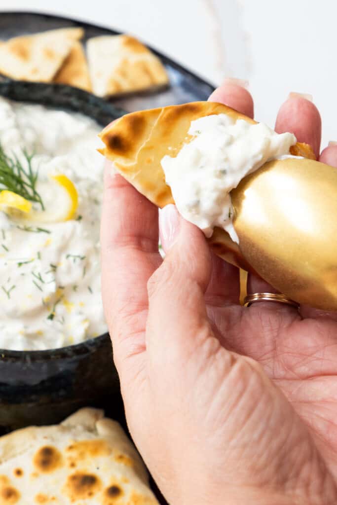 Tzatziki being spread onto pita bread with a gold spoon.