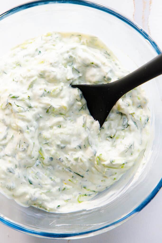 the mixed Tzatziki in a glass mixing bowl with a mixing spoon.