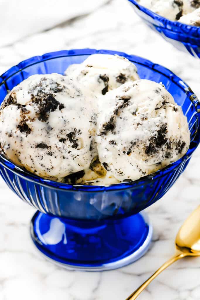 a blue glass ice cream bowl with three scoops of cookies and cream ice cream and a gold spoon.
