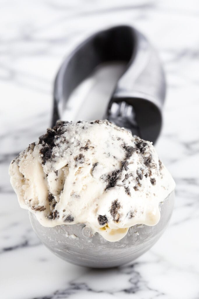a close up image of a ice cream scooper filled with cookies and cream ice cream.