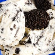a close up image of a blue glass dessert bowl with scoops of cookies and cream ice cream garnished with broken cookies.