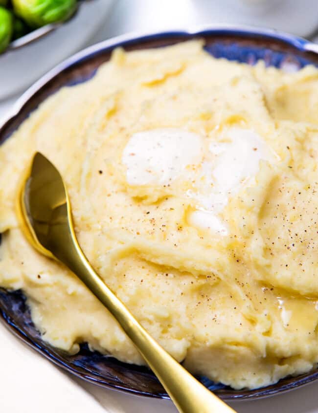 a close up image of a serving bowl of mashed potatoes topped with melting butter.
