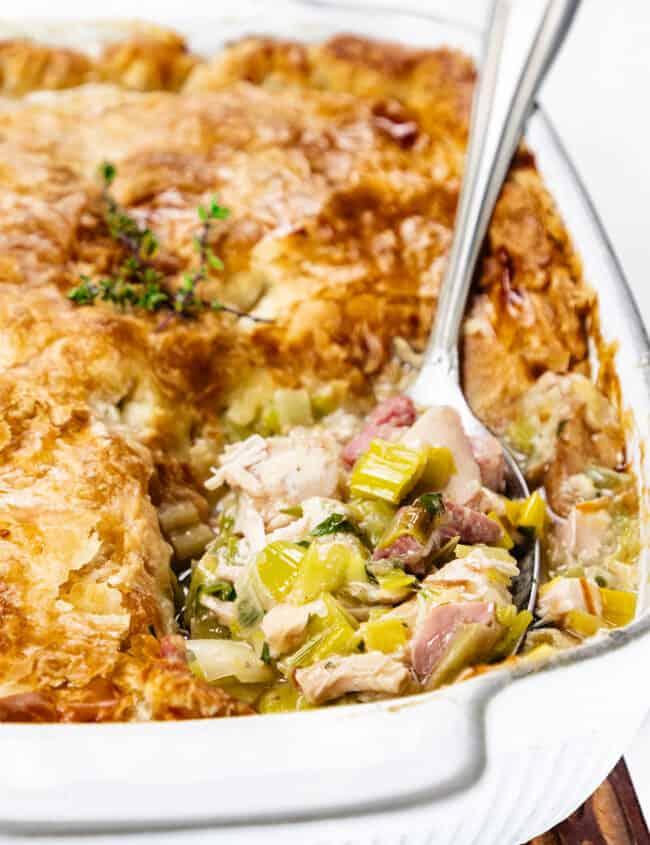 a close up image of Turkey and Ham Pie with a serving spoon full of a scoop of turkey, ham and leek filling.