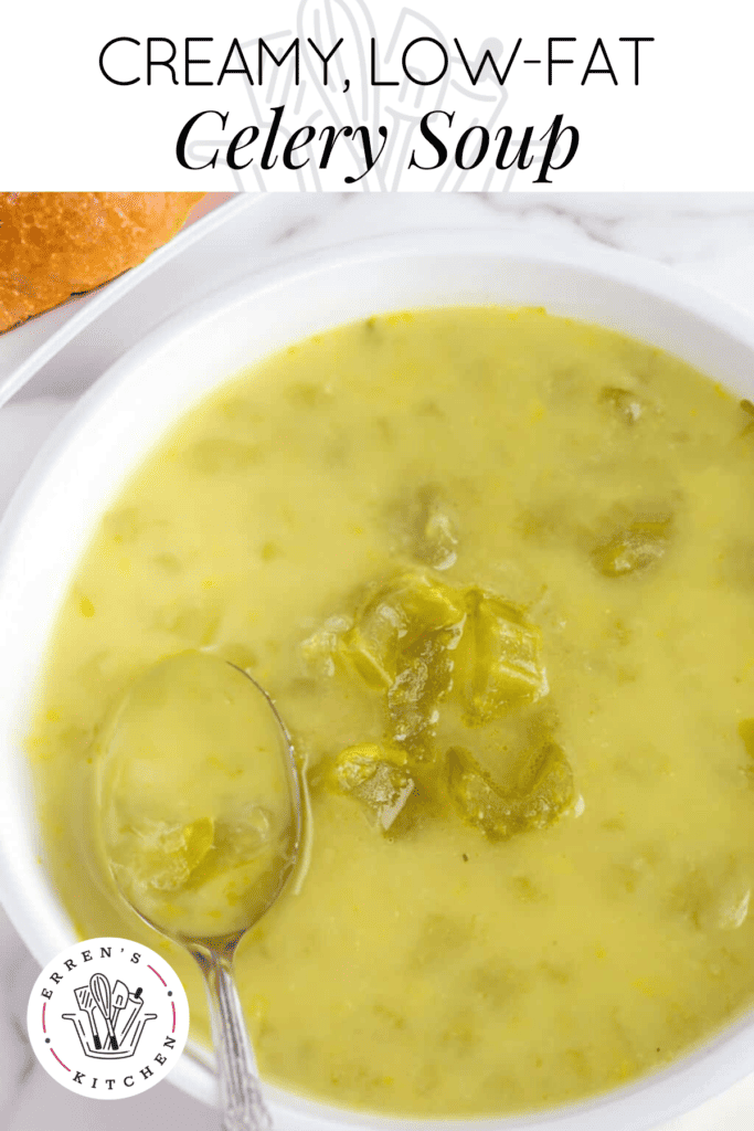 A close-up of a bowl of chunky celery soup with a spoon, showing the texture of the soup with pieces of celery visible, accompanied by a crusty bread roll on the side.