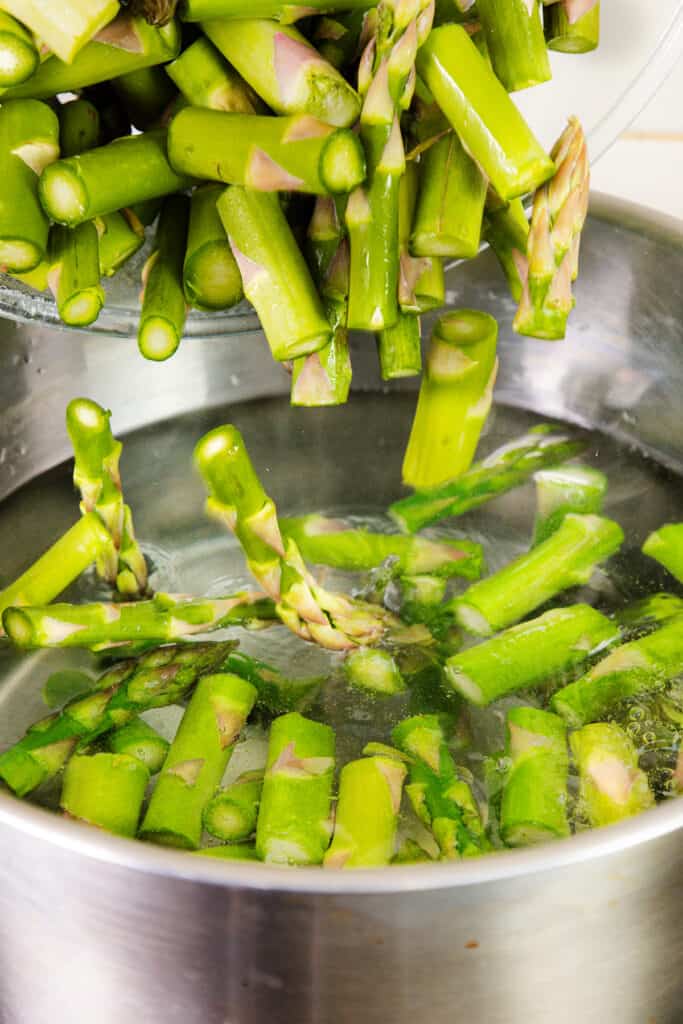 Asparagus being added to a pot of boiling water.