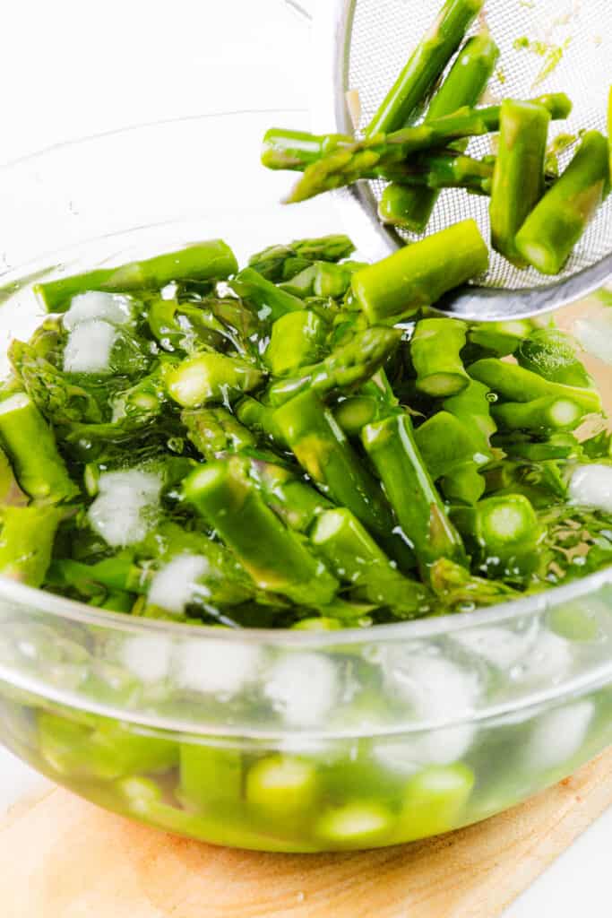 Asparagus being added to a bowl of ice water.