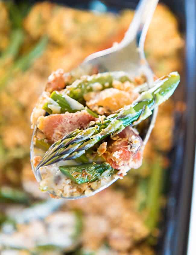 Close-up of a creamy asparagus casserole in a black dish, with a spoonful of the creamy filling with asparagus and bits of bacon.