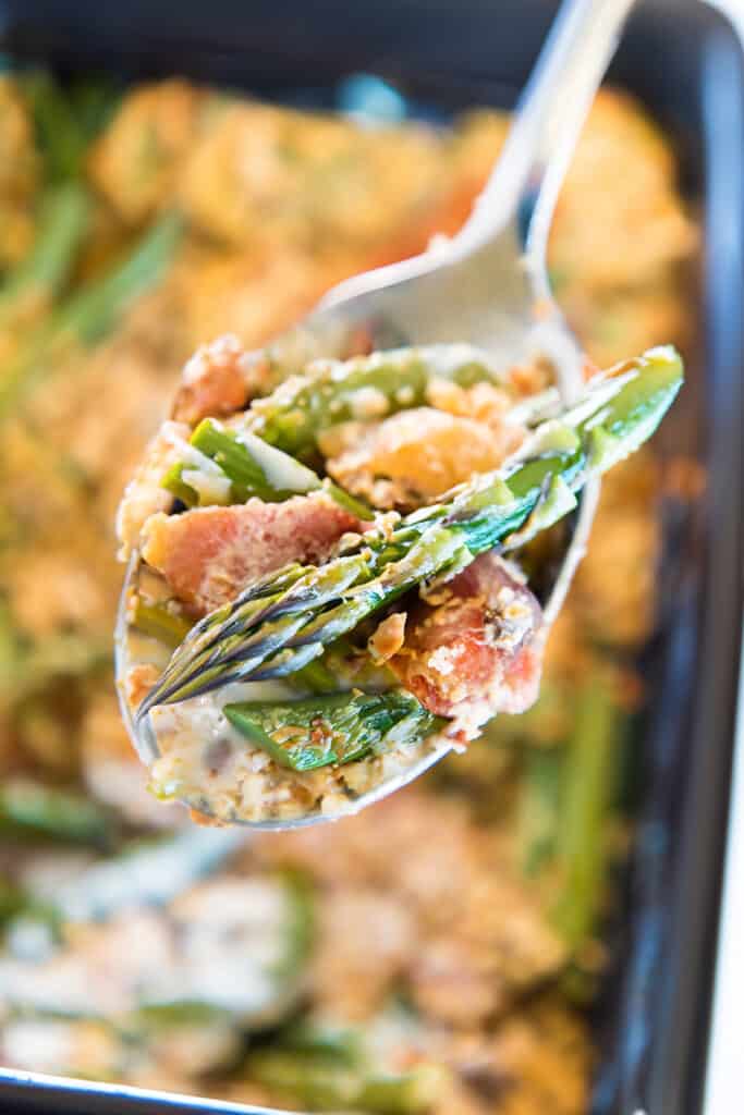 Close-up of a creamy asparagus casserole in a black dish, with a spoonful of the creamy filling with asparagus and bits of bacon.