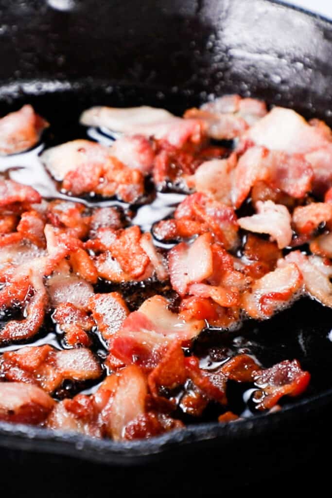 a close up photos of chopped bacon cooking in a black skillet.