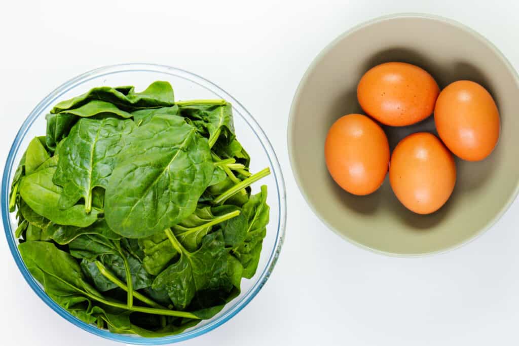 A bowl of fresh spinach and a bowl with 4 brown eggs.