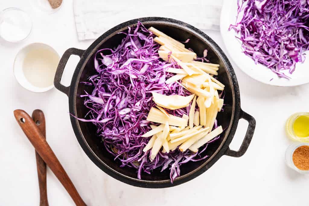 Shredded purple cabbage and sliced apple added to the pan with the onions.