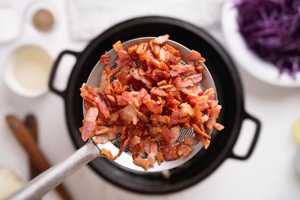 A slotted spoon removing crispy bacon from a pot.