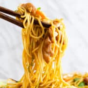 Chopsticks holding a twist of chicken lo mein with noodles, vegetables, and chicken, set against a blurred background.