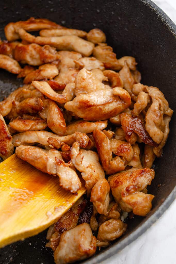 Sautéed chicken strips in a black skillet with a wooden spatula.