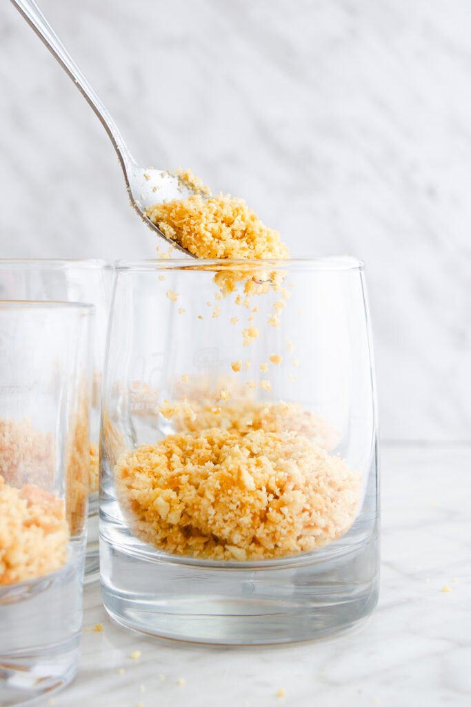 A spoonful of crushed graham cracker being poured into a glass.