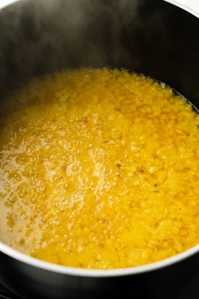 Red lentils cooking in a pot, showing bubbles forming on the surface as they simmer.