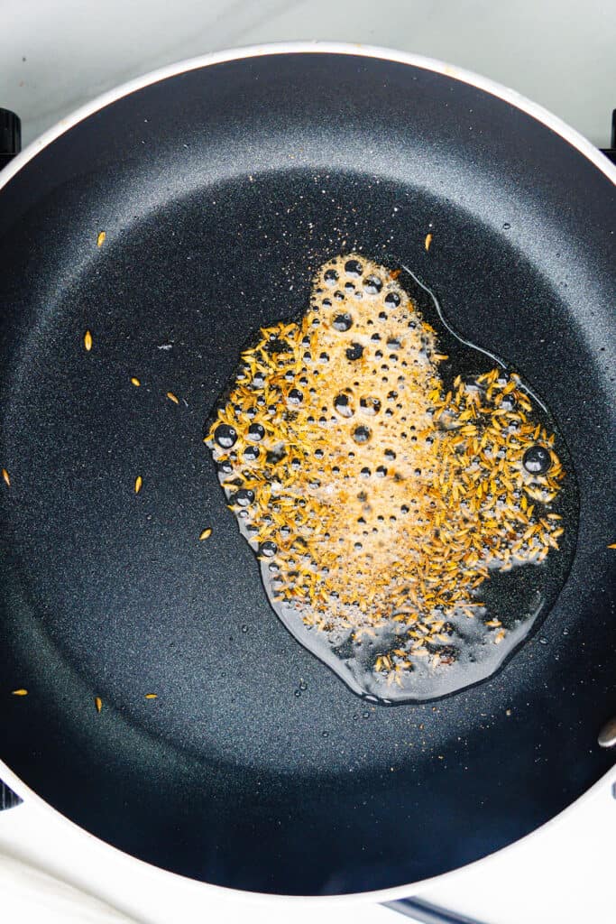 Cumin seeds and asafetida crackling in oil in a non-stick pan.