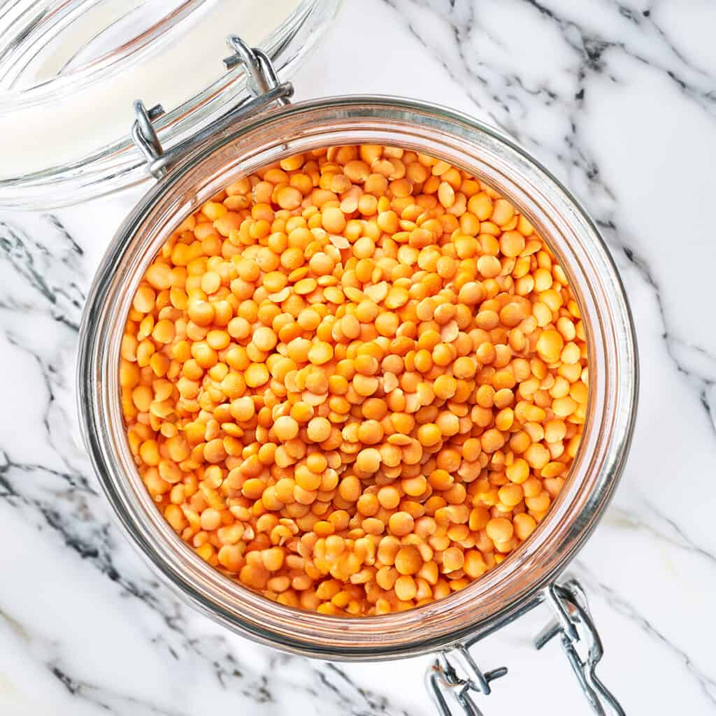 A glass jar full of red lentils on a marble countertop.