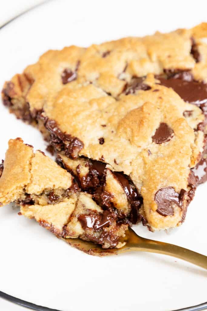 Close-up of a warm, sliced Pizookie with melted chocolate chunks oozing out, placed on a white plate with a golden fork.