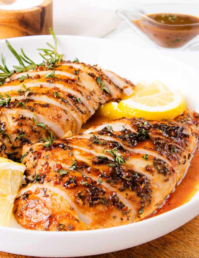 The image shows a juicy turkey tenderloin, sliced and served with rosemary and lemon, covered in a herby sauce. It looks well-cooked and tasty.