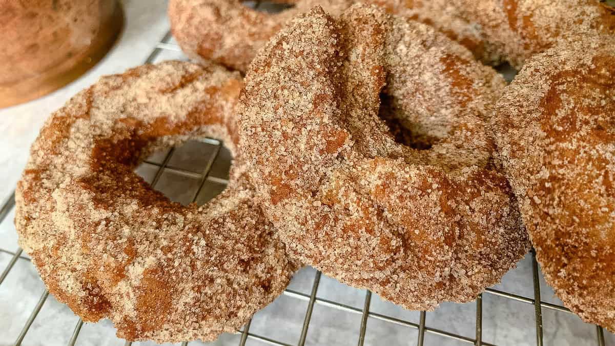 A close-up photo of a group of donuts covered in cinnamon sugar resting on a wire rack.