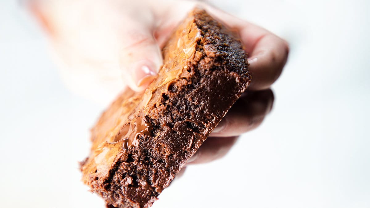 A close up image of a woman's hand holding a fudgy Chocolate Chip Chip Brownie.