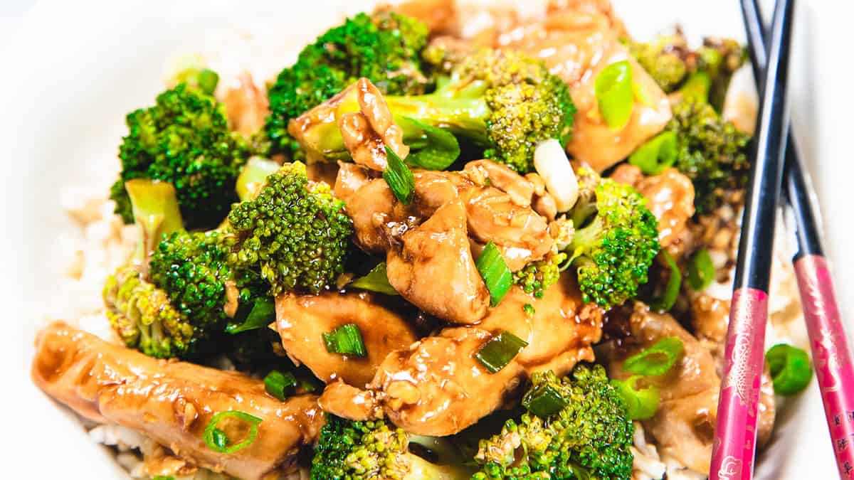 A chicken and Broccoli stir fry piled high on a white plate with chop sticks