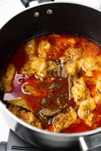 Chicken simmering in a spiced curry sauce in a black pot.